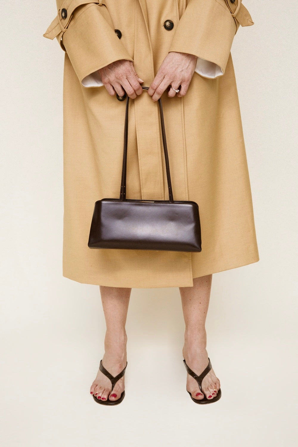 Person wearing a beige trench coat holding a Chocolate Éclair Clutch Shoulder Handbag on a plain background