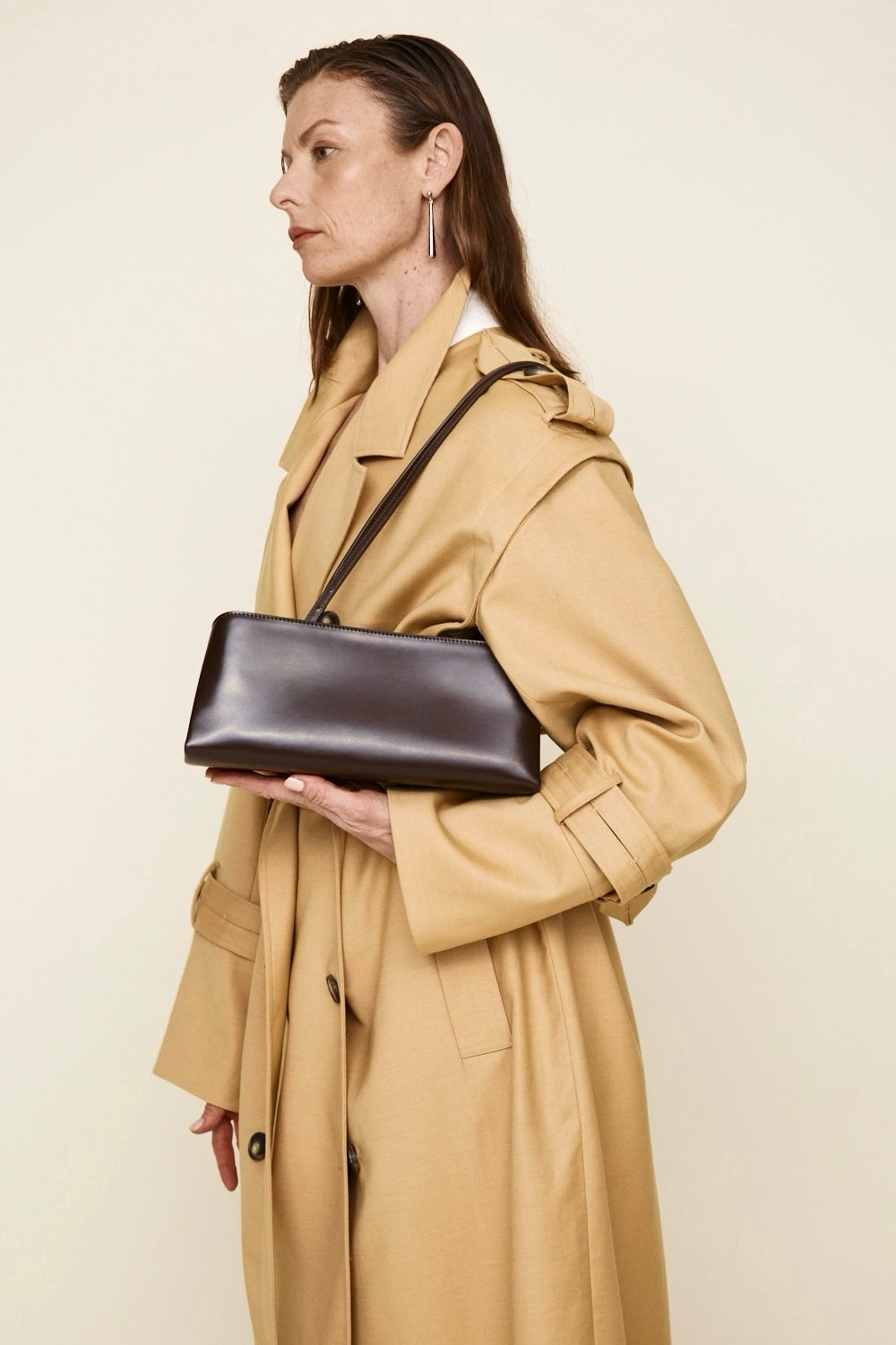 Woman in a beige trench coat holding a Chocolate Éclair Clutch Shoulder Handbag against a plain background
