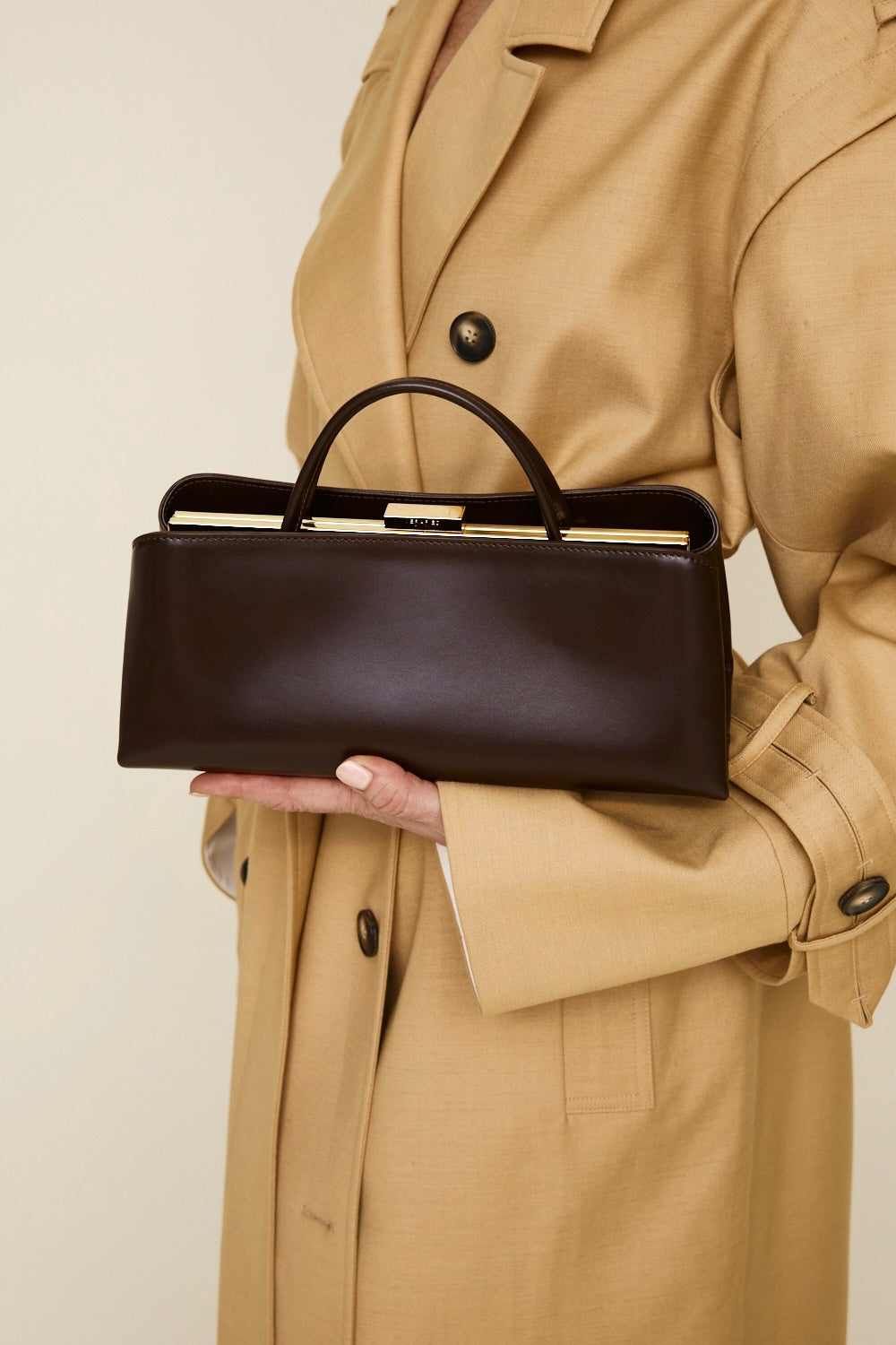 Person holding a Chocolate Éclair Clutch Shoulder Handbag wearing a beige trench coat against a neutral background