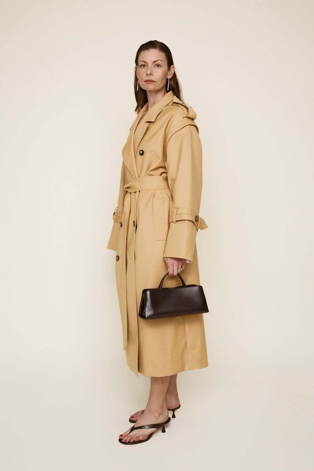 Woman wearing a beige trench coat holding a Chocolate Éclair Clutch Shoulder Handbag on a white background