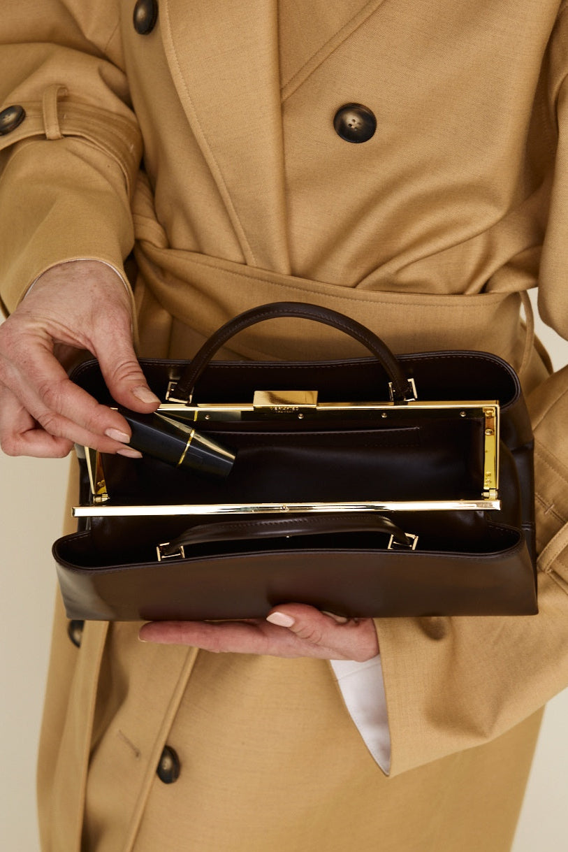 Person wearing a beige trench coat holding a Chocolate Éclair Clutch Shoulder Handbag with gold accents.