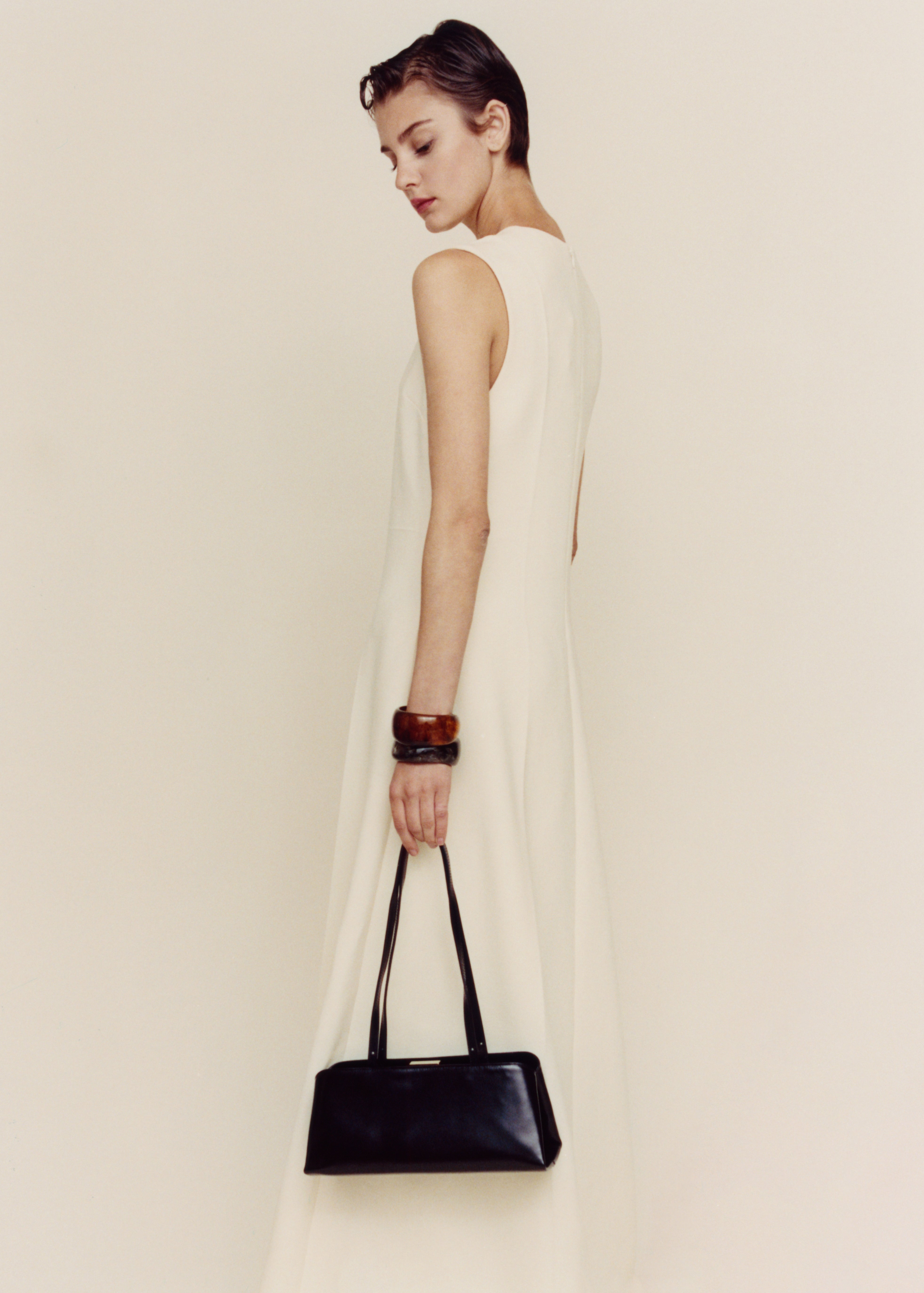 Woman in a white dress holding a Gold Noir Éclair Clutch Shoulder Handbag (Black) against a plain background