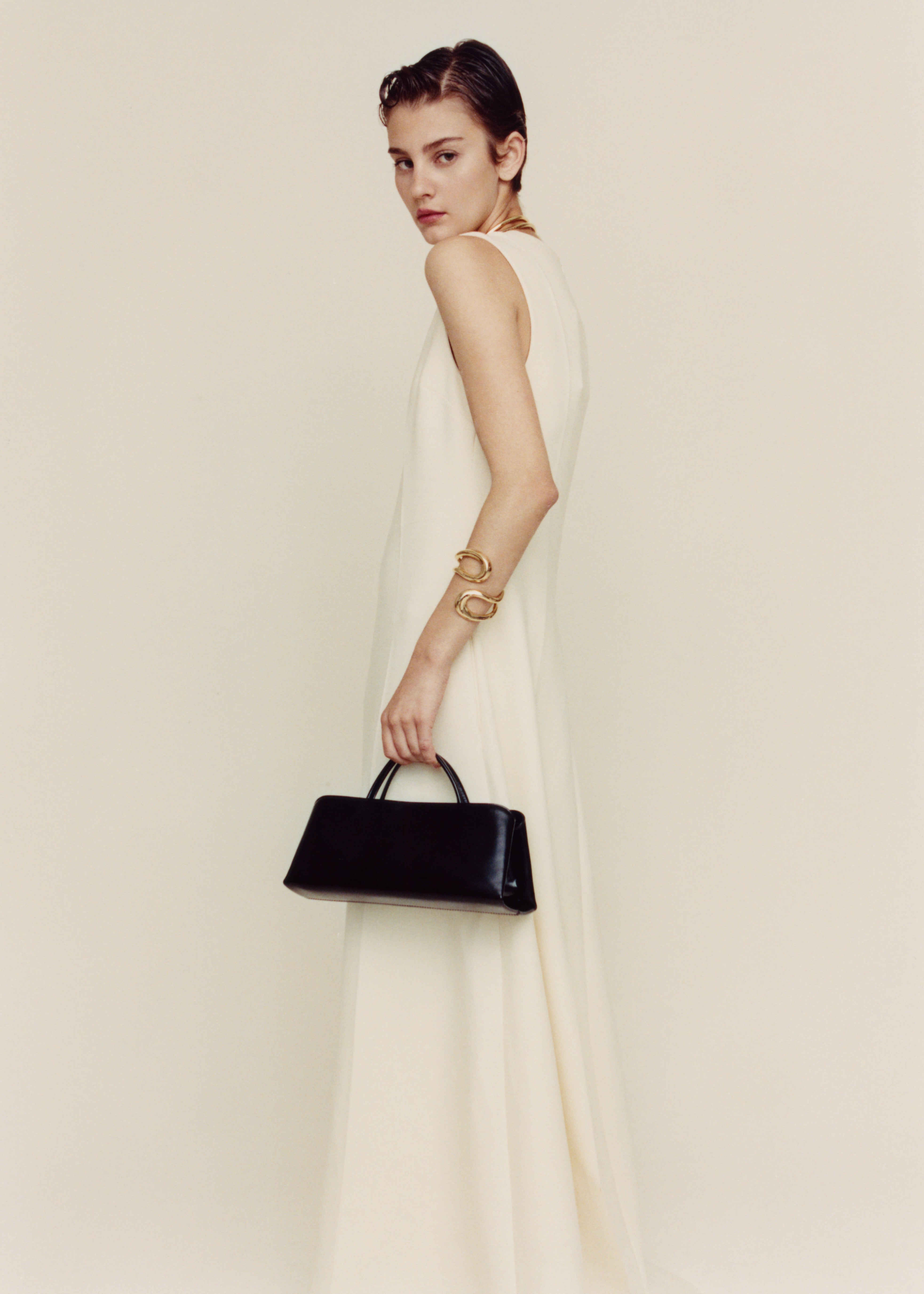 Woman in a long white dress holding a Gold Noir Éclair Clutch Shoulder Handbag (Black) against a plain background