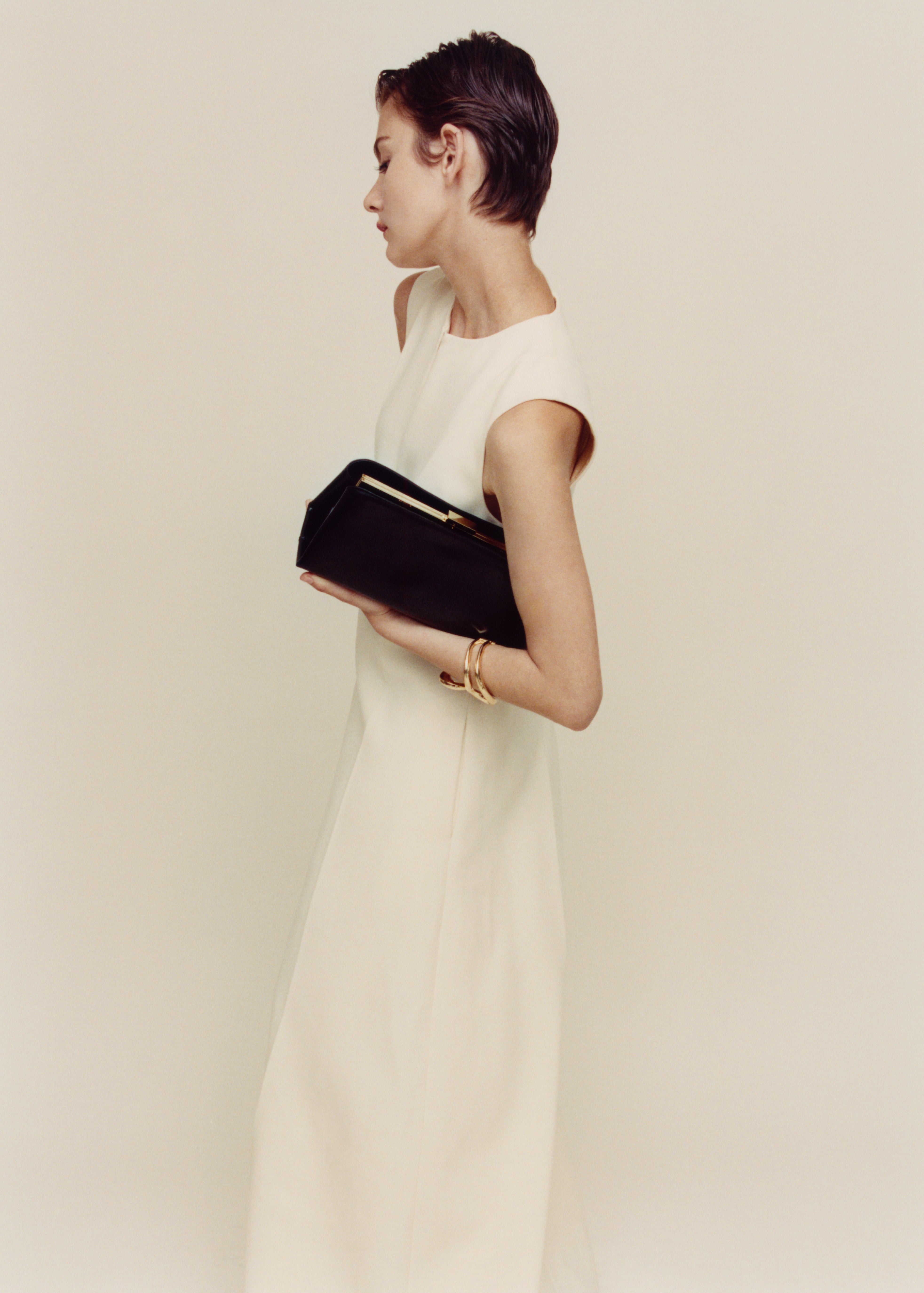 Woman in a white dress holding a Gold Noir Éclair Clutch Shoulder Handbag (Black) against a plain background