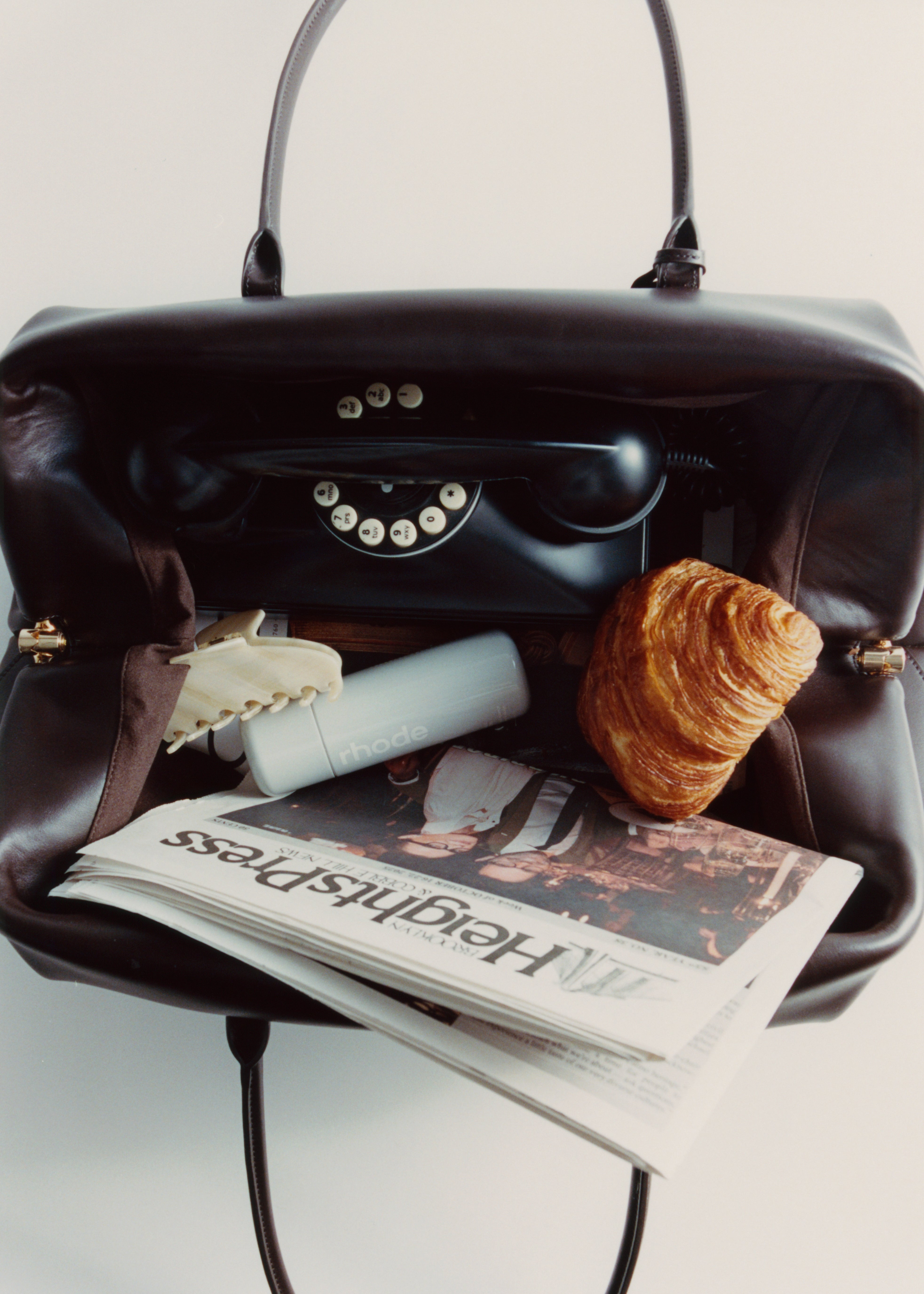 Chocolate Club Large Handbag with a newspaper, croissant, and phone inside on a light gray background