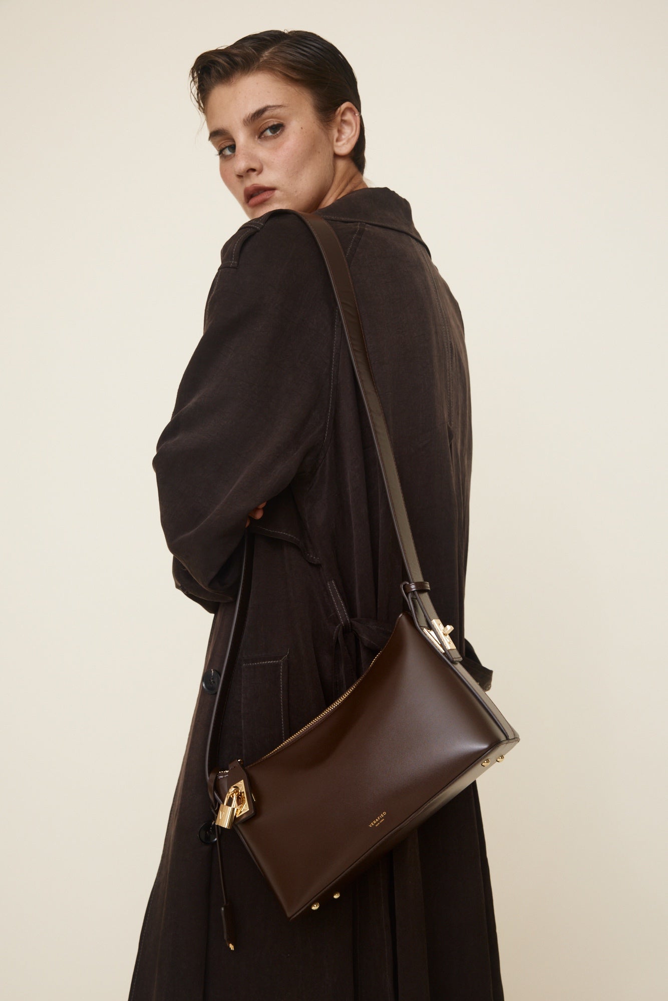 Woman wearing a dark coat with a Gold Chocolate Hobo Shoulder Handbag on a plain background