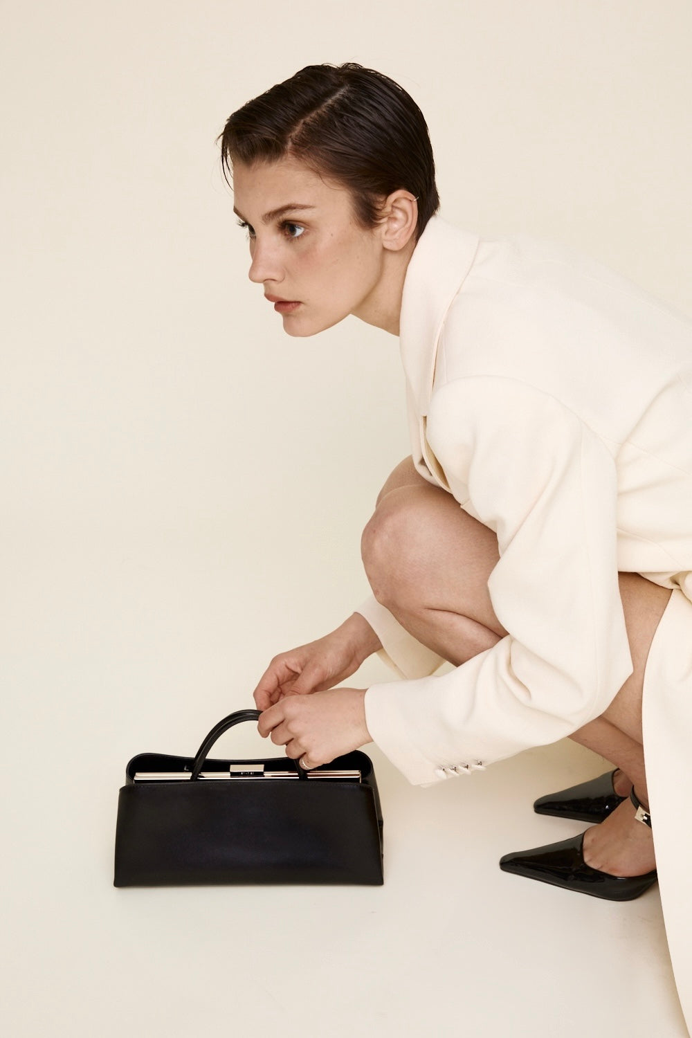Woman in a white outfit holding a Silver Noir Éclair Clutch Shoulder Handbag (Black) on a plain background