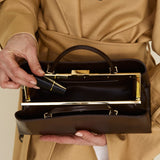 Person wearing a beige trench coat holding a Chocolate Éclair Clutch Shoulder Handbag with gold accents.