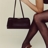 Person wearing brown high heels and holding a Chocolate Éclair Clutch Shoulder Handbag against a neutral background