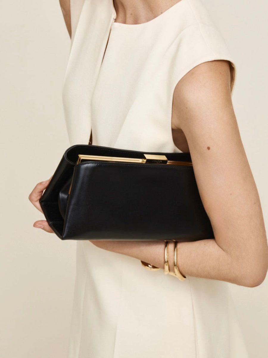 Person holding a Gold Noir Éclair Clutch Shoulder Handbag (Black) with gold accents against a neutral background