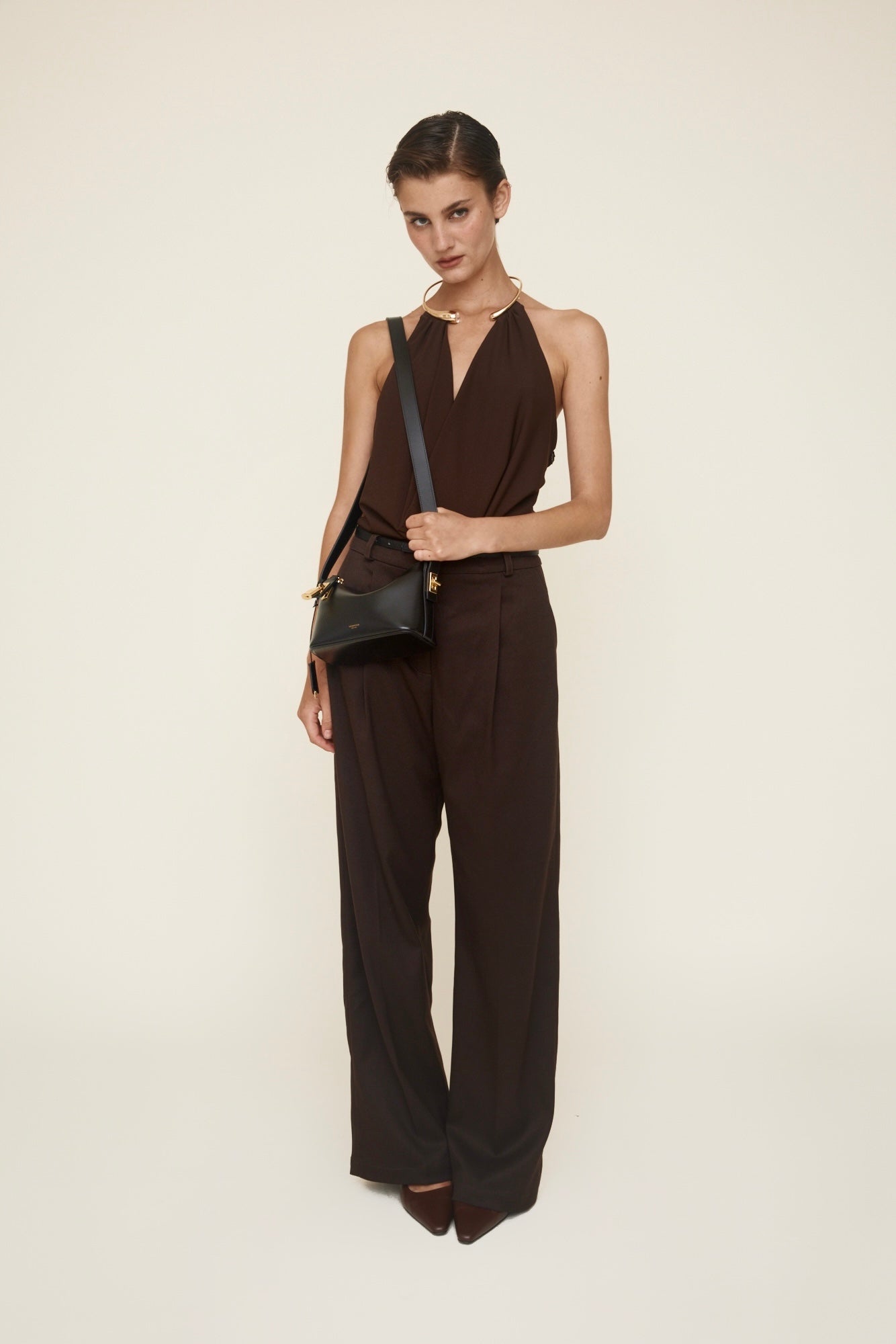 Woman wearing a brown jumpsuit holding a Mini Gold Black Hobo Shoulder Handbag on a white background