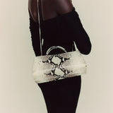 Person wearing a black off-shoulder top and holding a Python Éclair Clutch Shoulder Handbag with black snake print pattern.