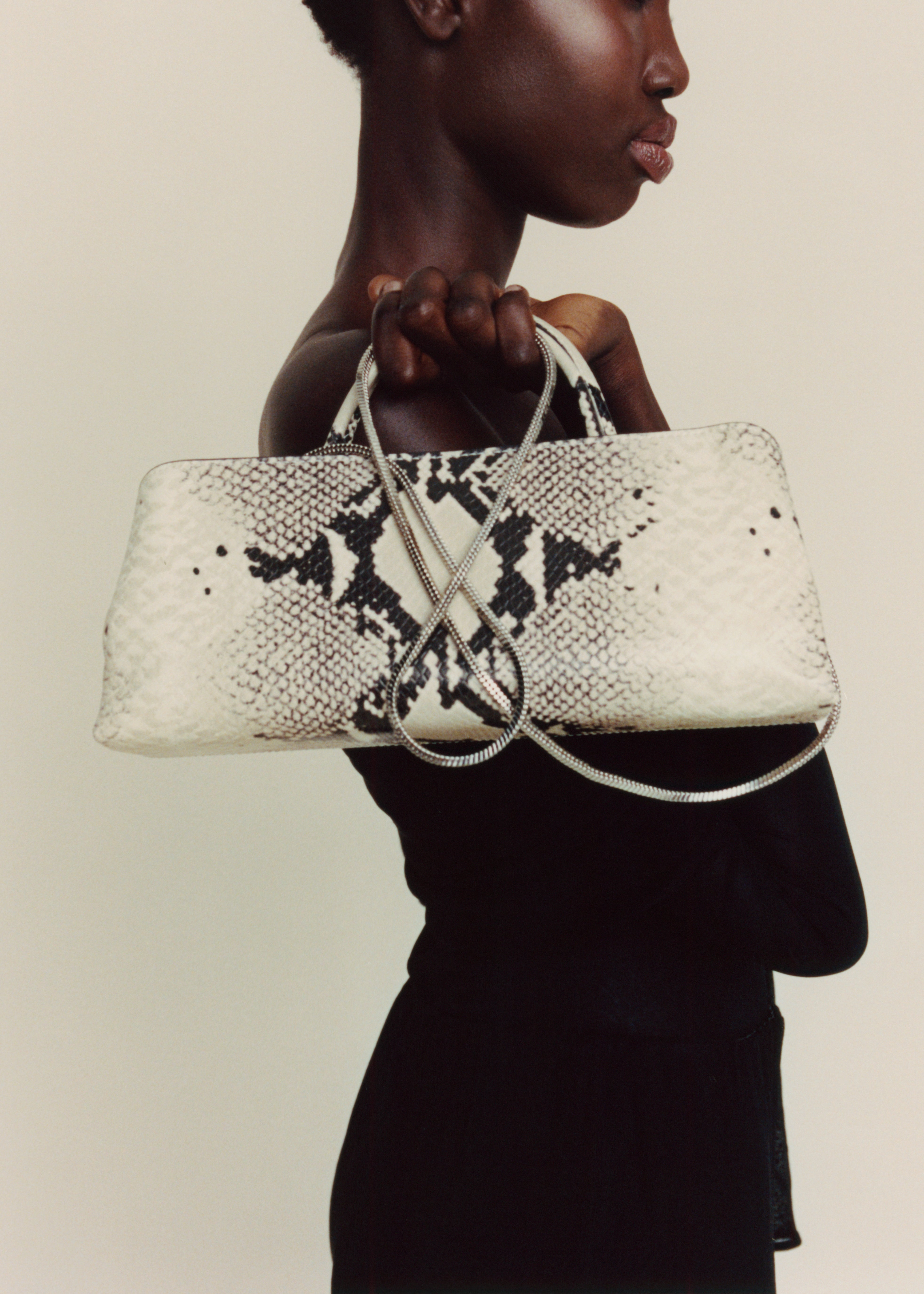 Woman holding a Python Éclair Clutch Shoulder Handbag with black snake print pattern against a beige background