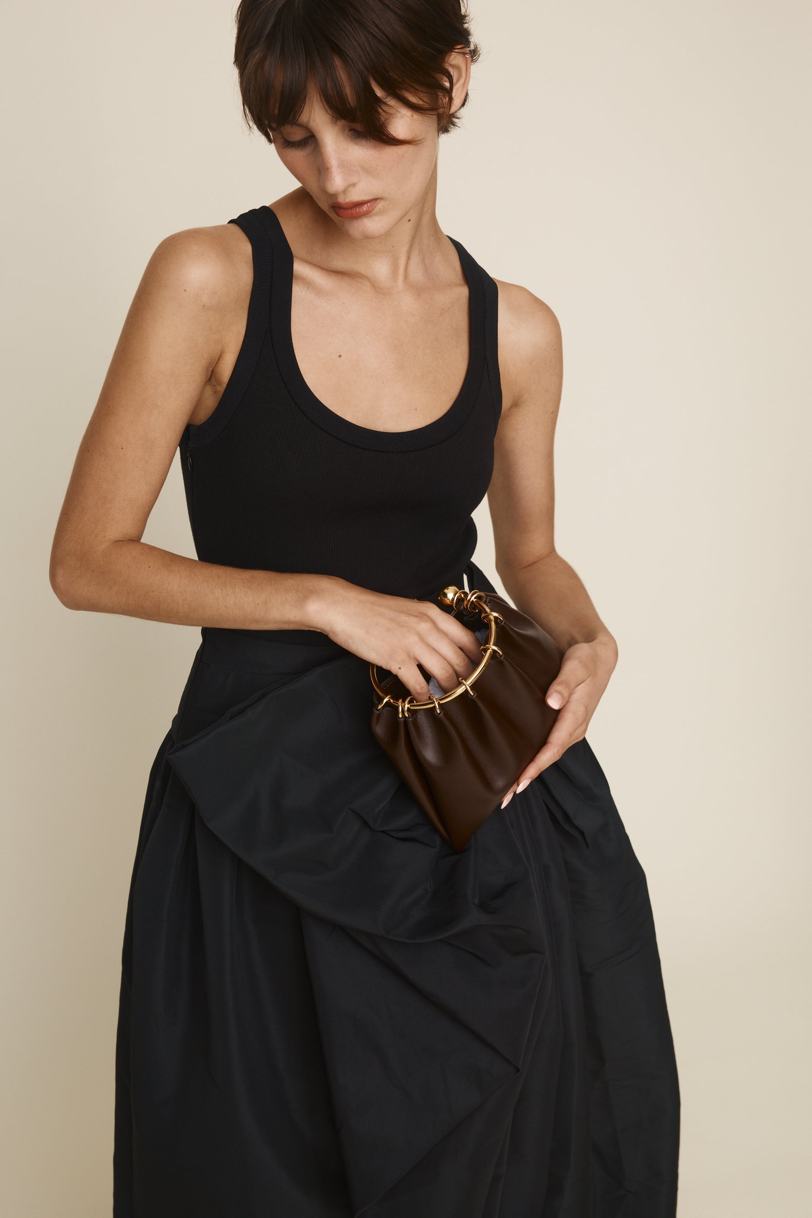 Woman holding a Chocolate Circle Ring Mini Handle Bag against a beige background