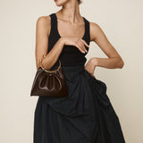 Woman holding a Chocolate Circle Ring Mini Handle Bag wearing a black dress against a beige background