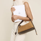 Woman holding a brown Gold Suede Hobo Shoulder Handbag and a white folder against a plain background