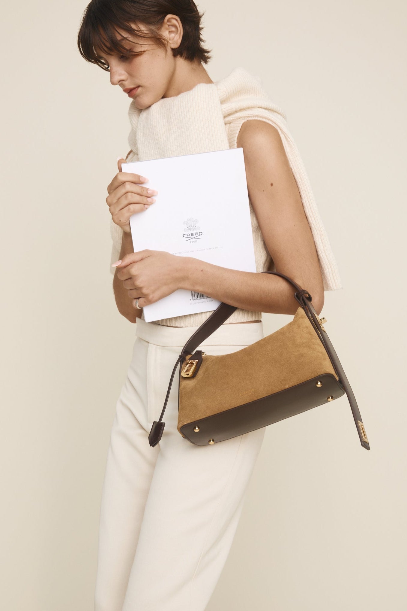 Woman holding a brown Gold Suede Hobo Shoulder Handbag and a white folder against a plain background