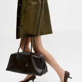 Person wearing a green coat and brown shoes, holding a Chocolate Club Large Handbag on a white background