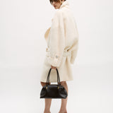 Person wearing a white coat and holding a Chocolate Medium Club Shoulder Handbag on a white background