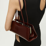 Burgundy Clutch Shoulder Handbag held by a person wearing a black dress on a light gray background
