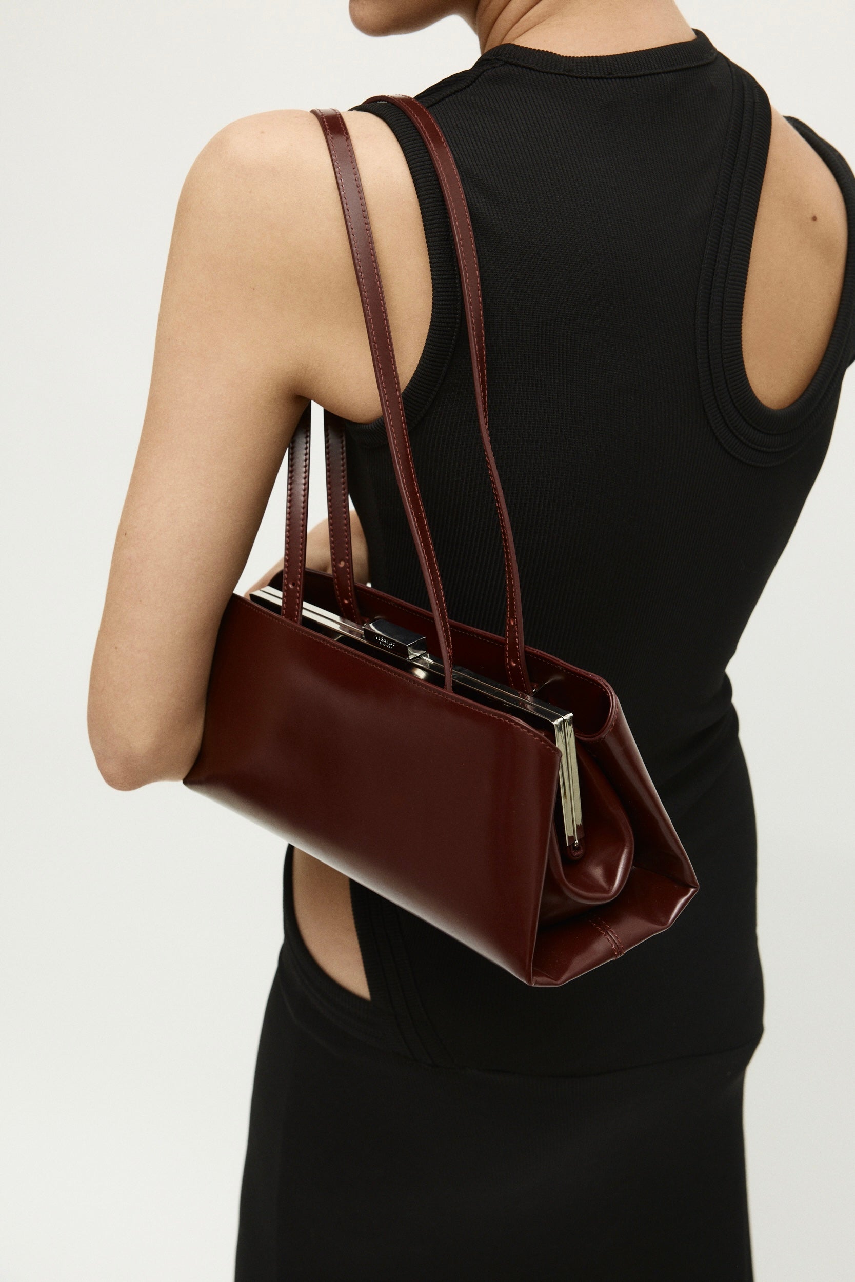 Burgundy Clutch Shoulder Handbag held by a person wearing a black dress on a light gray background