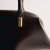 Close-up of a Chocolate Medium Club Shoulder Handbag with a gold clasp on a light gray background
