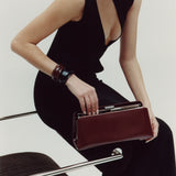 Woman in a black dress holding a Burgundy Clutch Shoulder Handbag against a white background