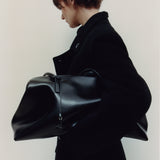 Person wearing a black coat holding a large Black Club Large Handbag against a plain background