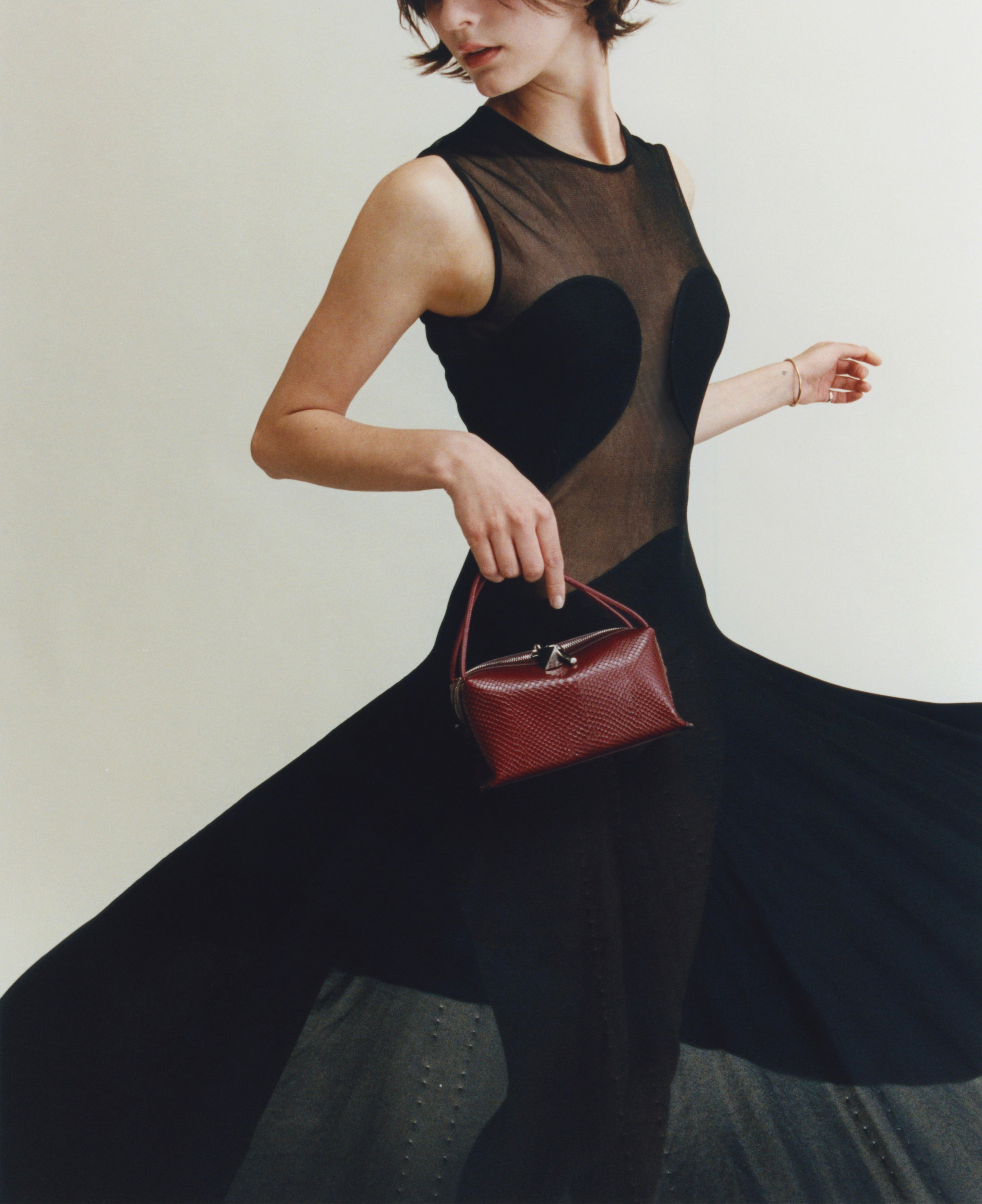 Woman holding a Maroon Python Café Mini Bag: Crossbody Handbag wearing a black dress with a heart design.