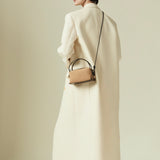 Person wearing a long cream coat holding a Verafied New York Gold Suede Café Mini Handbag against a plain background