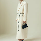 Person wearing a long white coat and black hat holding a Verafied New York Black Lizard Café Mini Handbag on a plain background