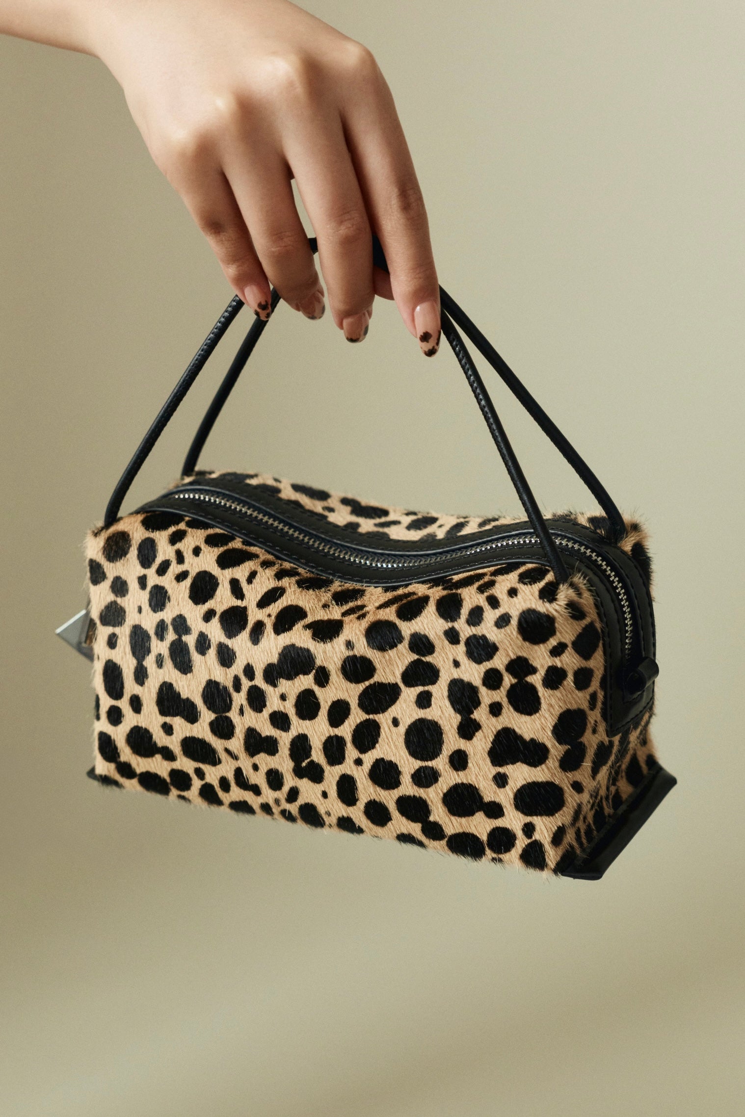 Leopard print Verafied New York Cheetah Calf Hair Café Mini Handbag held by a hand against a beige background