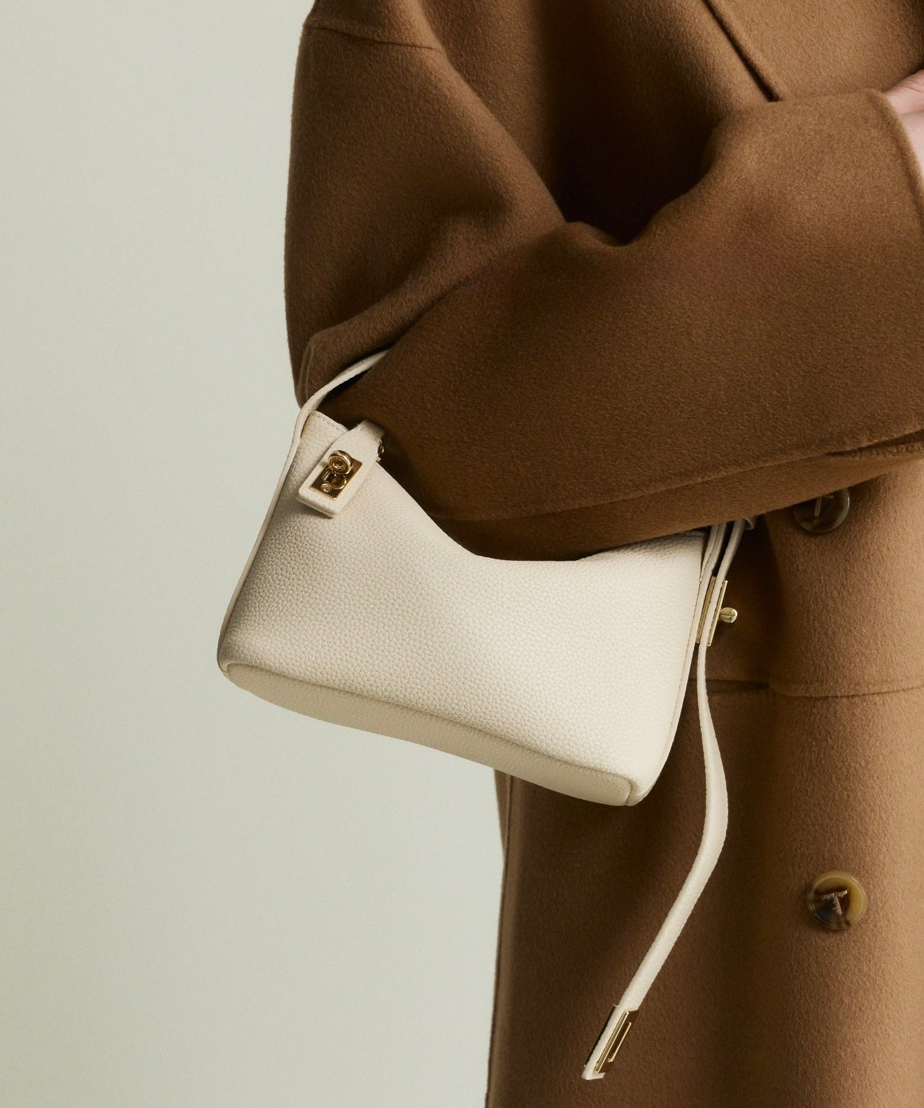 Person wearing a brown coat holding a white Ivory Twister Hobo Handbag against a neutral background