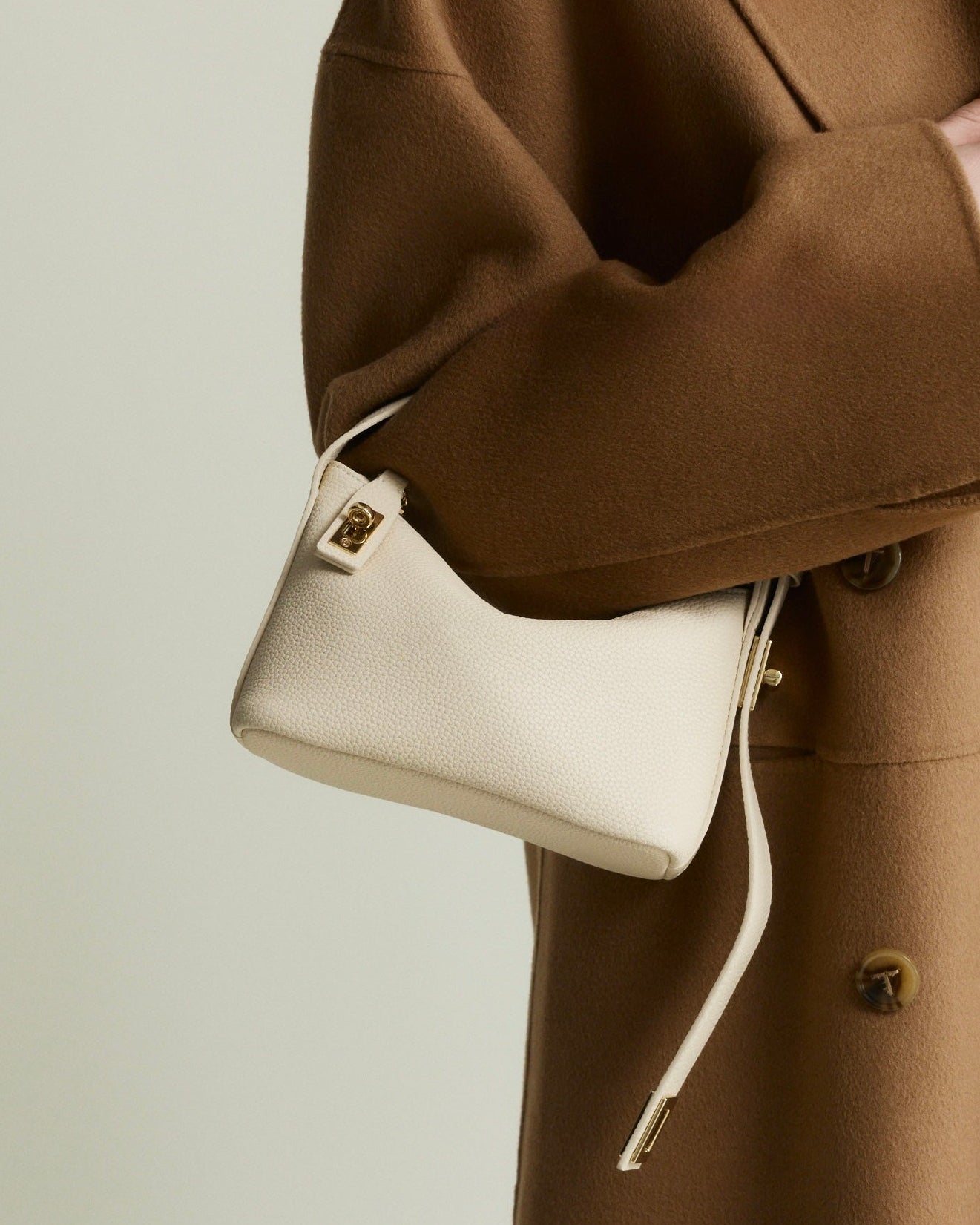 Person wearing a brown coat holding a white Ivory Twister Hobo Handbag against a neutral background