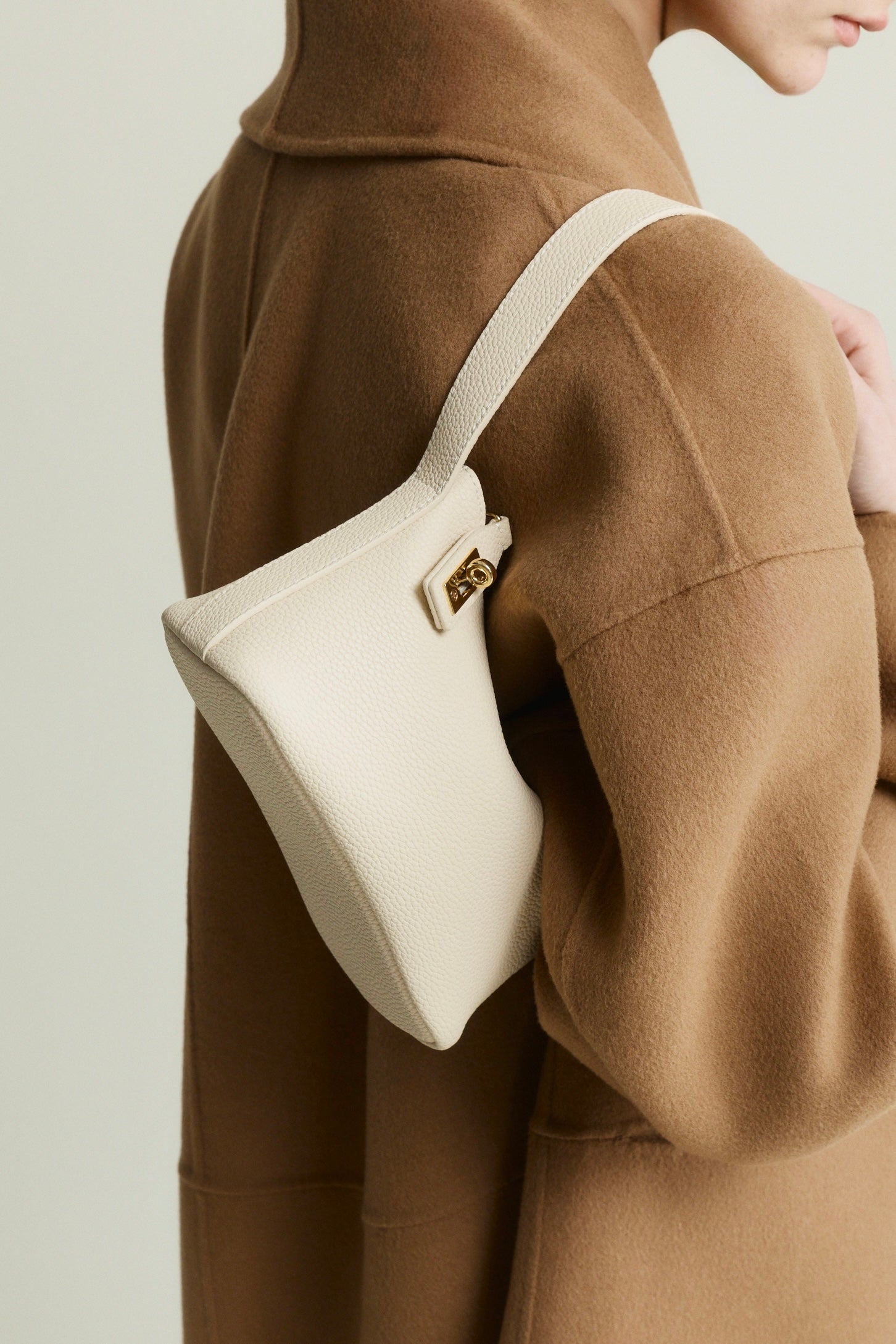 Person wearing a brown coat with a white Ivory Twister Hobo Handbag on a plain background