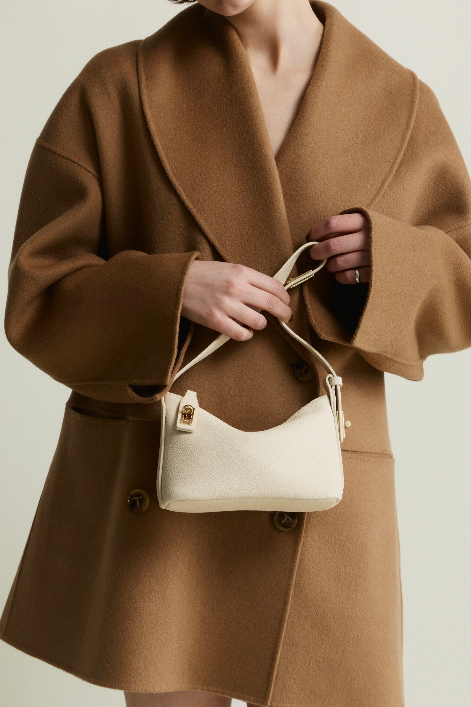 Person wearing a brown coat holding a Ivory Twister Hobo Handbag against a neutral background