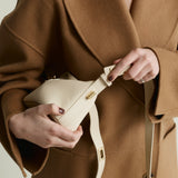 Person wearing a brown coat holding a Ivory Twister Hobo Handbag with a plain background