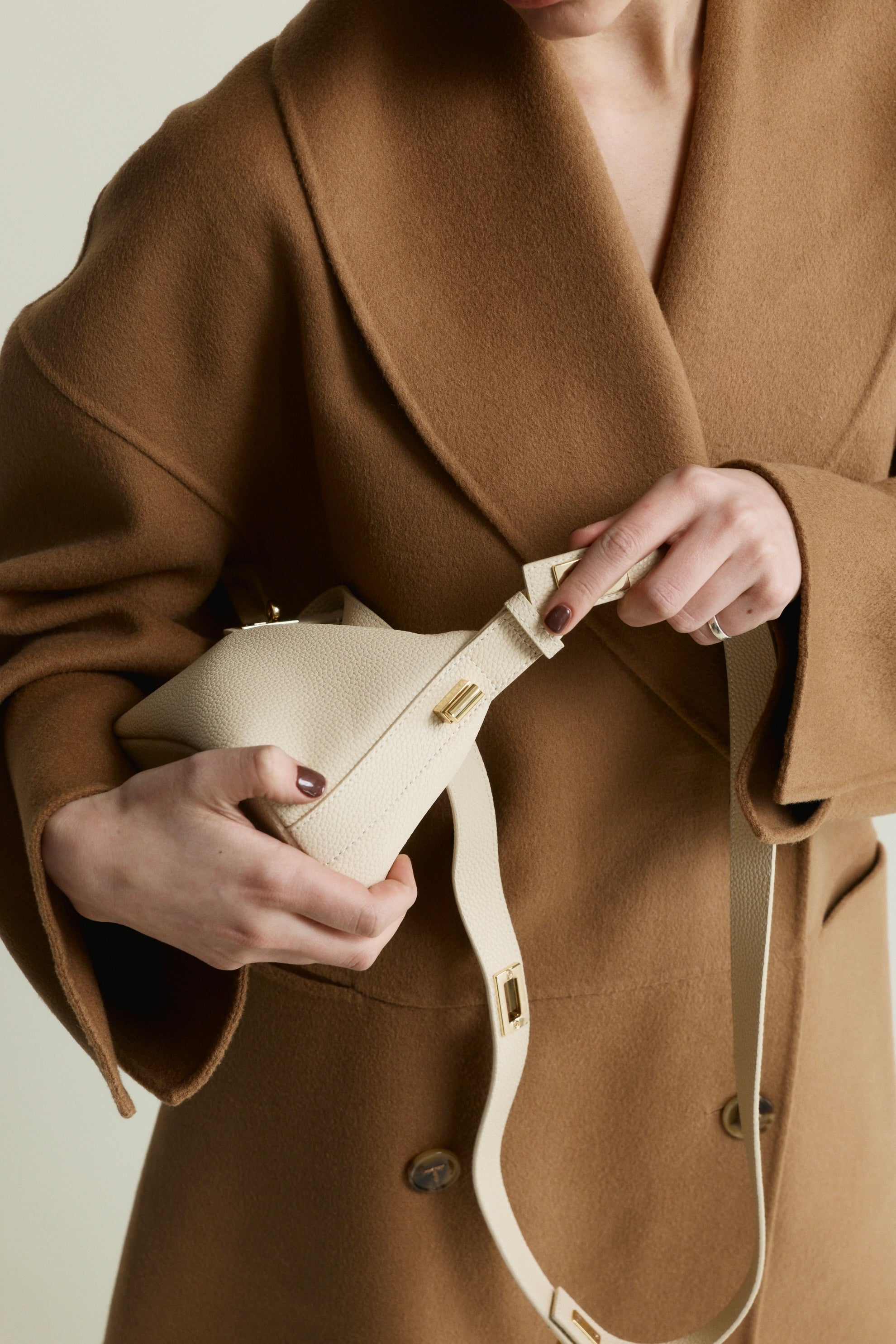 Person wearing a brown coat holding a Ivory Twister Hobo Handbag with a plain background