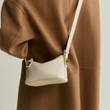Person wearing a brown coat with a white crossbody Ivory Twister Hobo Handbag n a neutral background