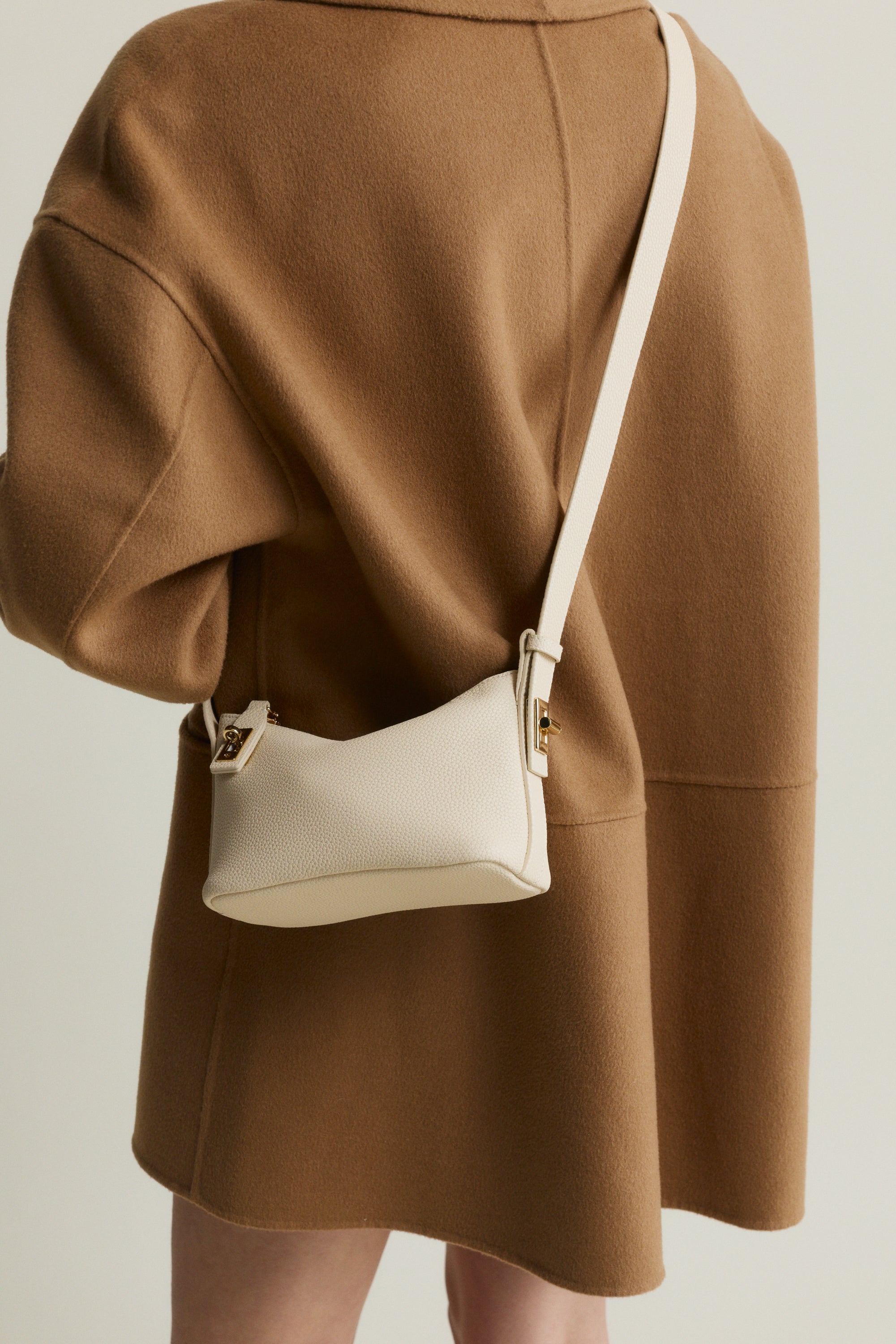 Person wearing a brown coat with a white crossbody Ivory Twister Hobo Handbag n a neutral background