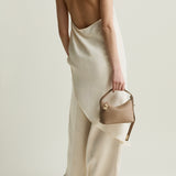 Person wearing a white dress with open back holding a beige Twister Hobo Shoulder Handbag on a plain background