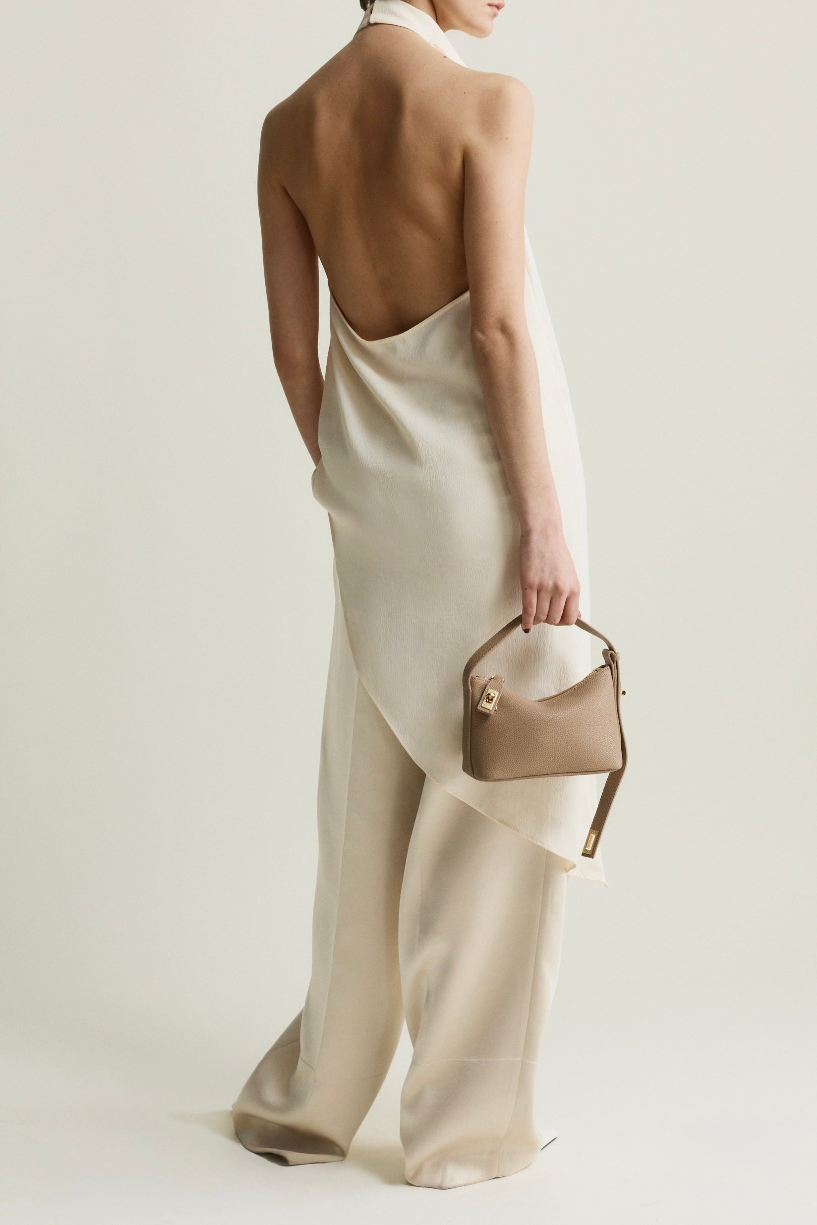 Person wearing a white dress with open back holding a beige Twister Hobo Shoulder Handbag on a plain background