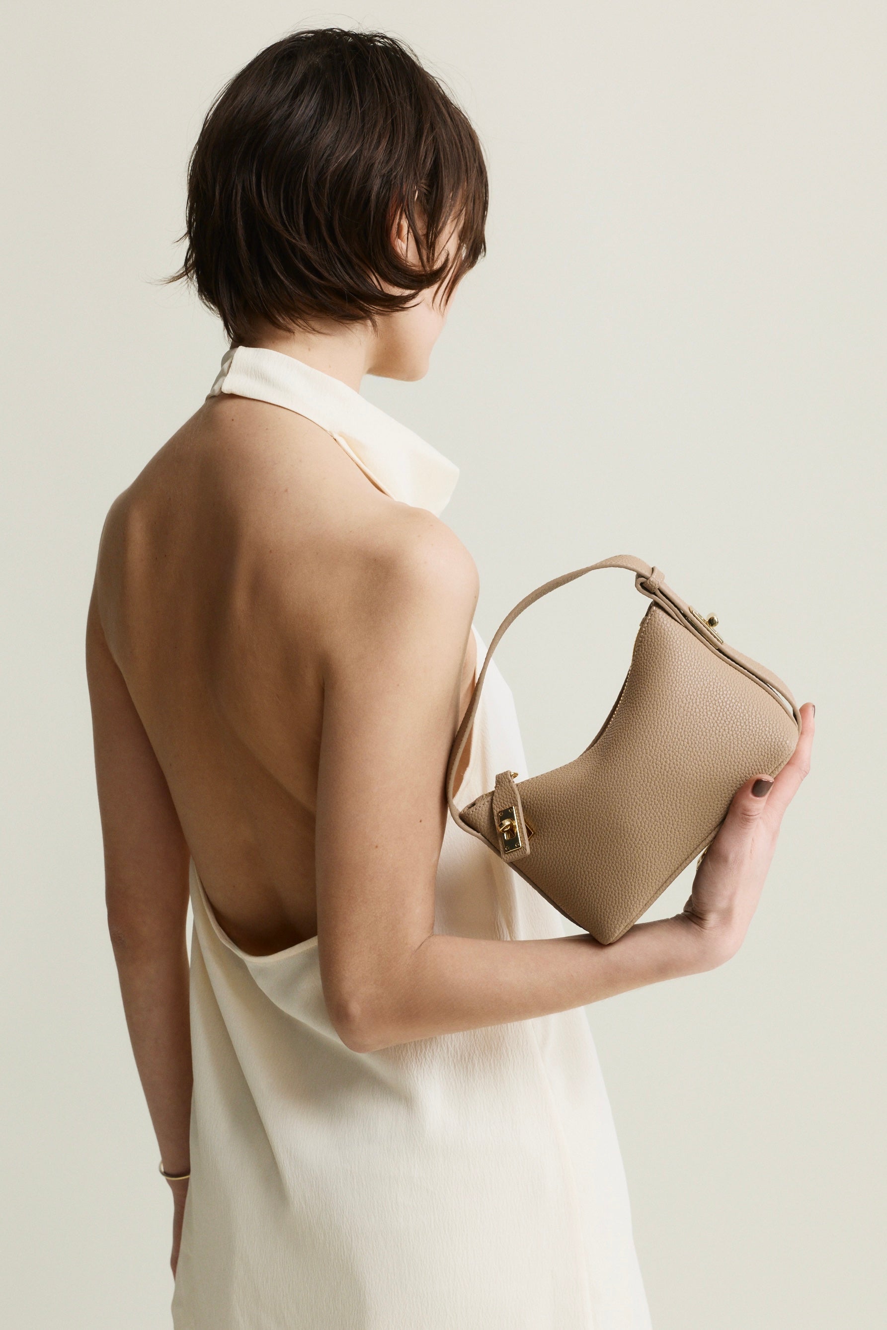 Woman holding a beige Twister Hobo Shoulder Handbag against a plain background