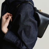 Person wearing a dark blue coat with a Mini Gold Black Hobo Shoulder Handbag on a neutral background