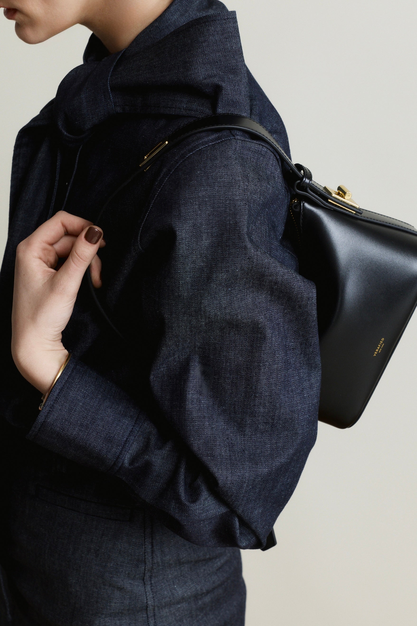 Person wearing a dark blue coat with a Mini Gold Black Hobo Shoulder Handbag on a neutral background
