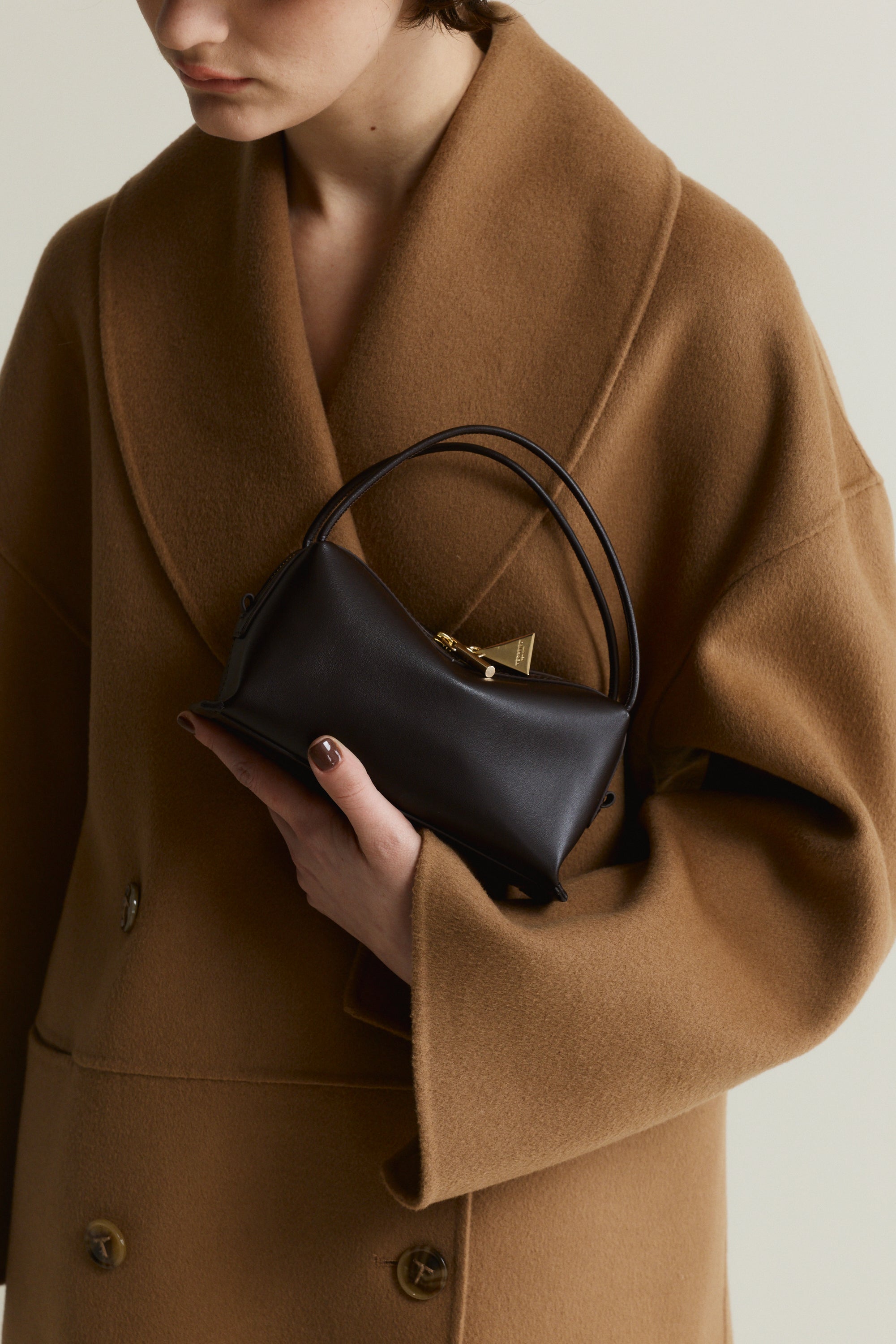 Person wearing a brown coat holding a Chocolate Café Mini Crossbody Handbag against a neutral background