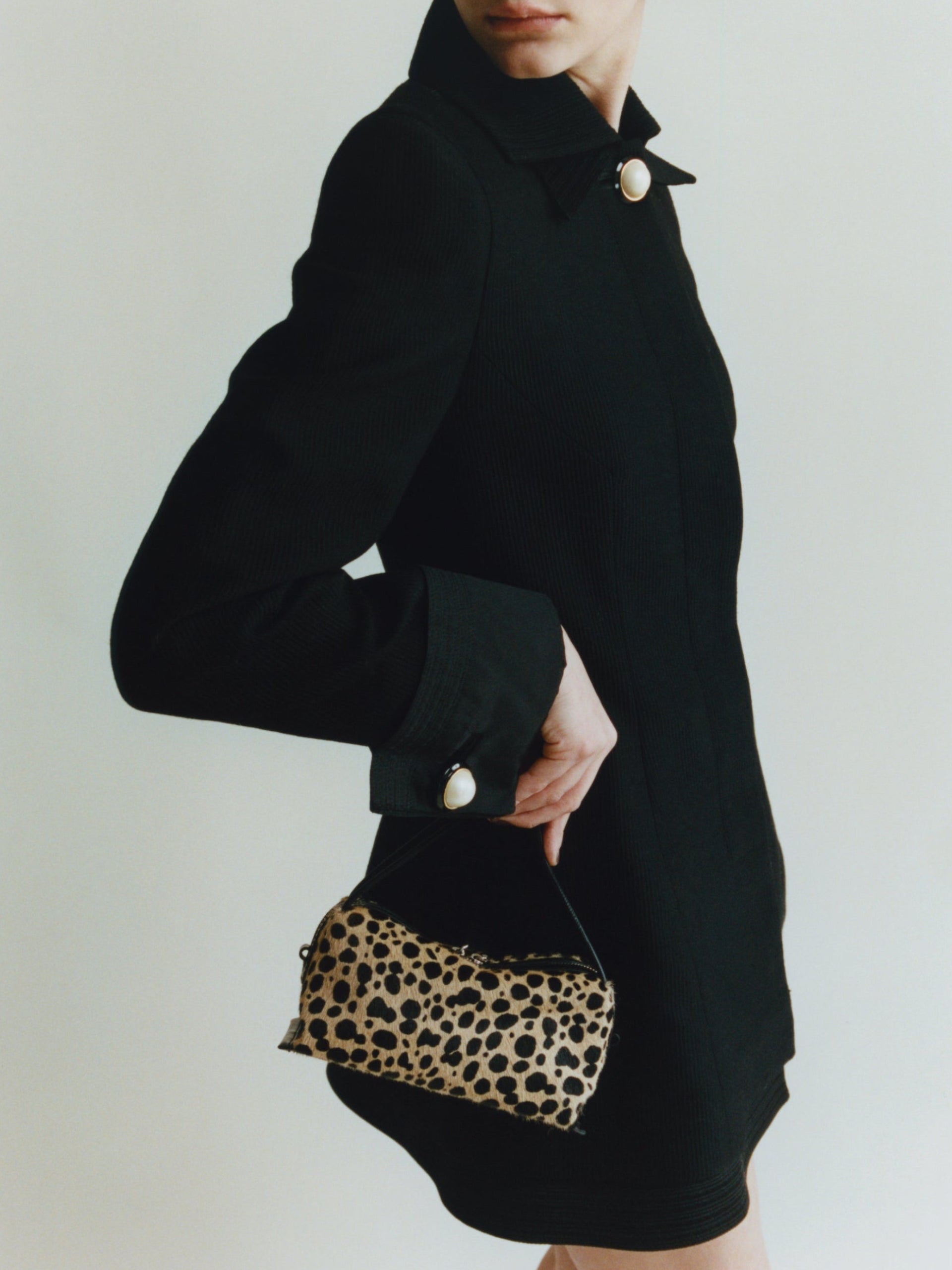 Person wearing a black dress holding a leopard print Cheetah Calf Hair Café Mini Crossbody Handbag against a plain background