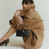 Person wearing a brown coat holding a Chocolate Café Mini Crossbody Handbag on a white background