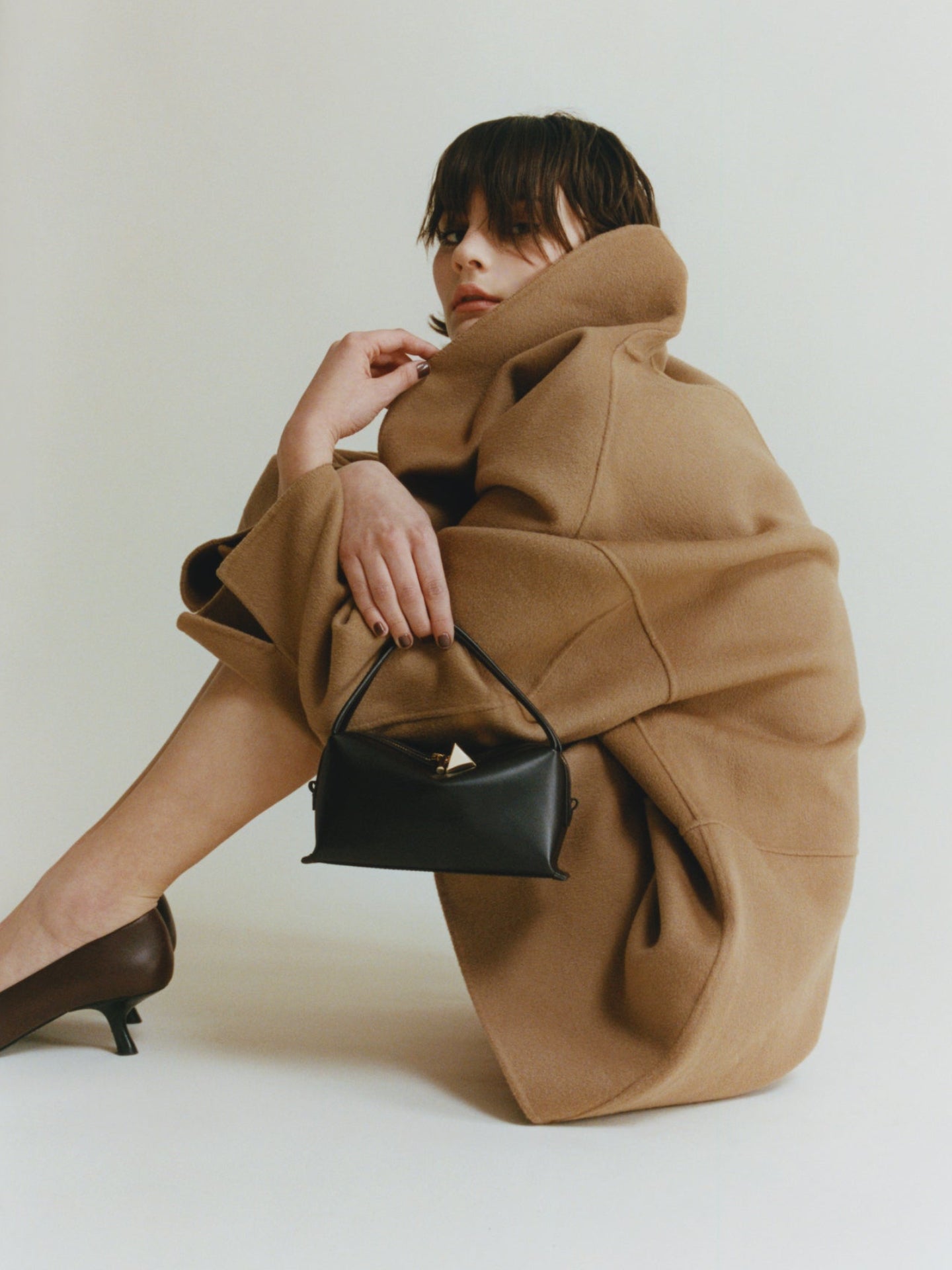 Person wearing a brown coat holding a Chocolate Café Mini Crossbody Handbag on a white background