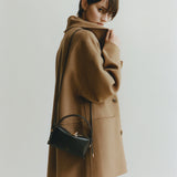 Person wearing a brown coat holding a Chocolate Café Mini Crossbody Handbag against a plain background